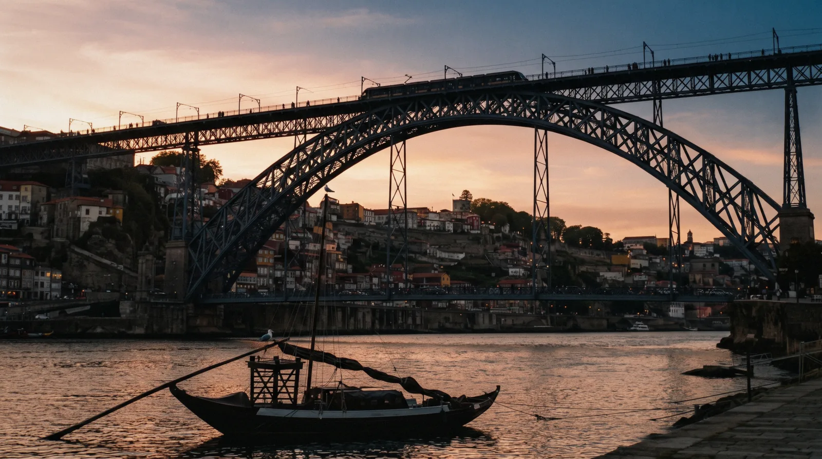 The iron arch of the Luís I bridge from the Gaia quay at 18:40, a yellow metro train crossing the upper deck and the Ribeira houses catching the last light behind it, Luís I bridge Porto