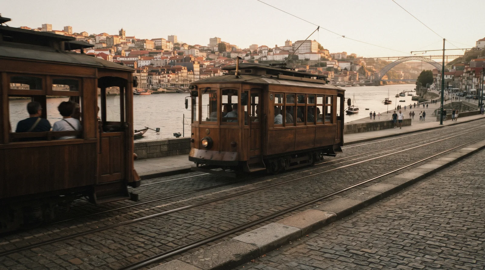 A varnished wooden heritage tram of line 1 running along the Douro quay at Massarelos at 17:40 with the river on one side, two passengers small at the open window, porto tram