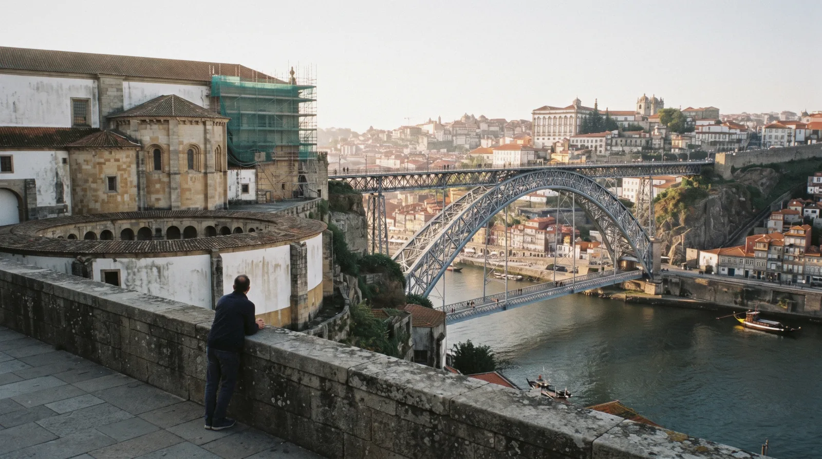The circular church and round cloister of Serra do Pilar on its bluff above the Douro at 08:30, the iron arch of the road bridge below and the Porto bank behind, one walker small on the terrace wall, serra do pilar