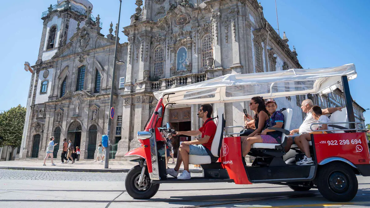 A red electric tuk-tuk carrying visitors past a baroque church in Porto