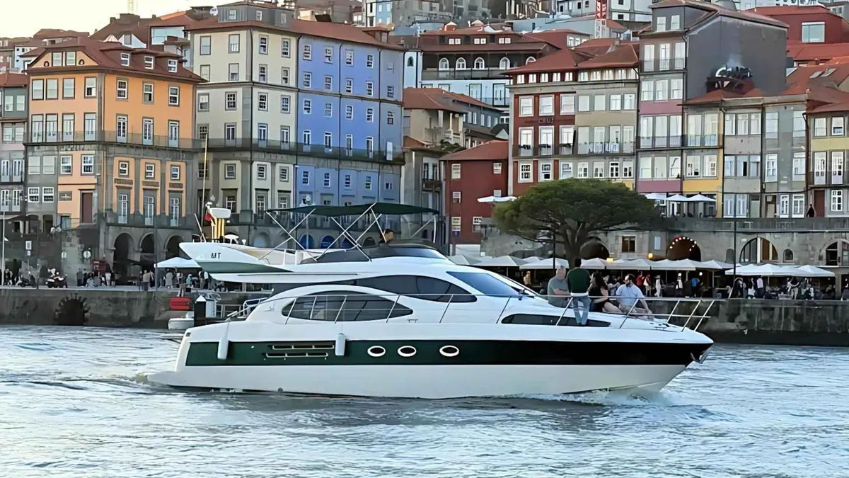 A white motor yacht cruising past the riverfront houses of Porto