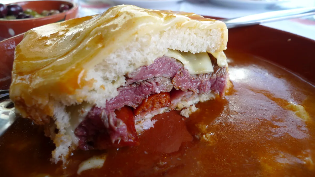 A francesinha cut open on the plate, layers of steak, sausage and ham under melted cheese and the tomato-and-beer sauce, the dish Porto is known for