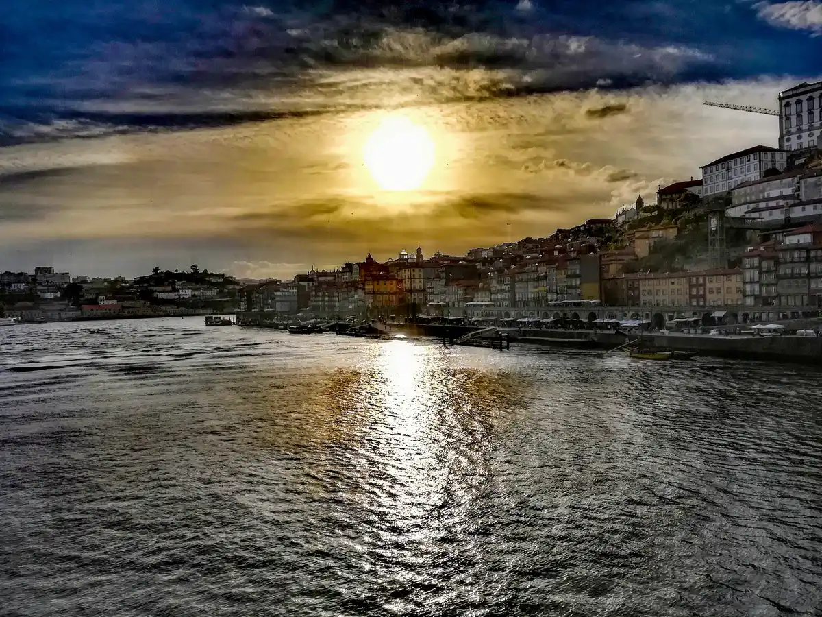 The Ribeira and the cathedral hill of Porto under a dark winter sky, the river grey and the houses lit by a break in the cloud