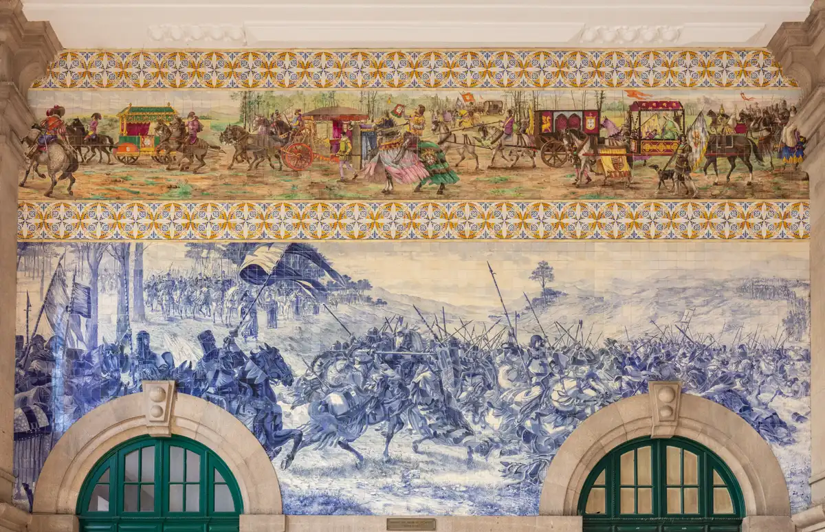 The azulejo-panelled hall of São Bento station in Porto, blue-and-white tile scenes around the departure board and the arched windows